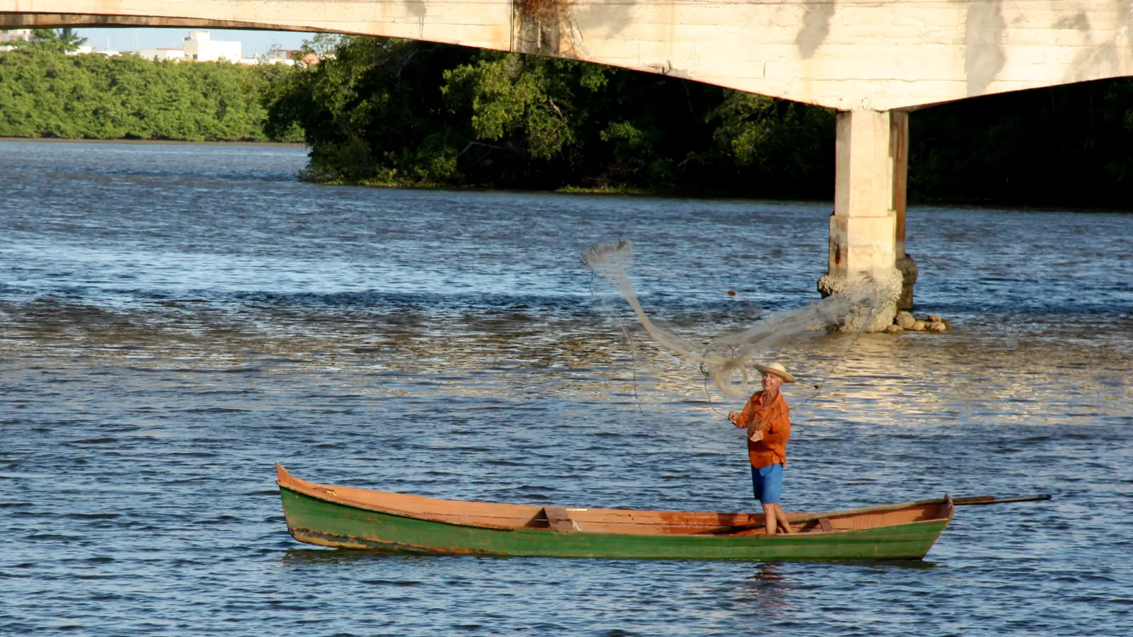 Pescador em canoa no Rio Poxim, sob uma ponte