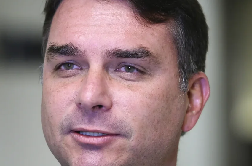 Retrato do senador Flávio Bolsonaro, de terno cinza e gravata amarela, durante entrevista