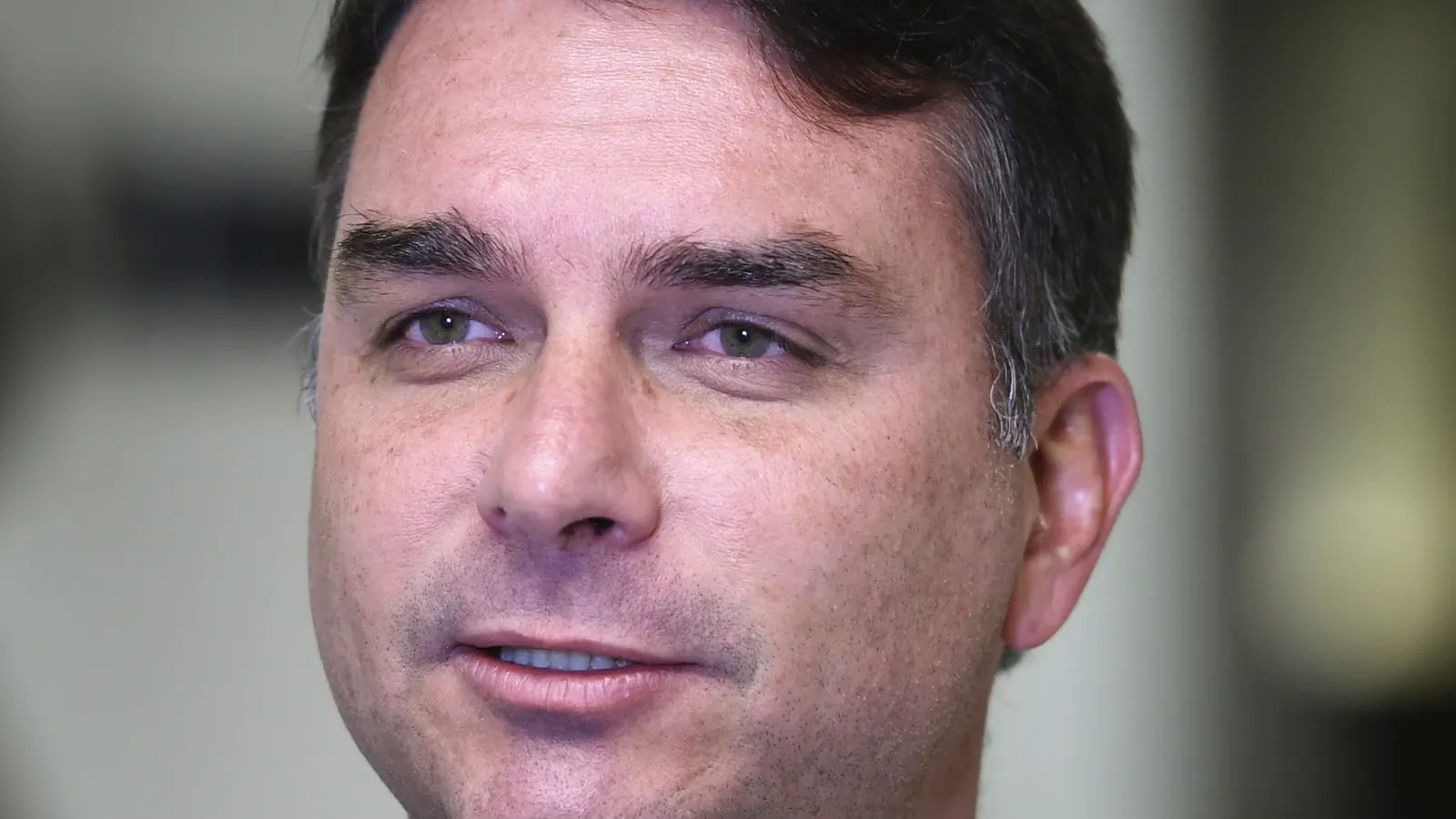 Retrato do senador Flávio Bolsonaro, de terno cinza e gravata amarela, durante entrevista